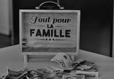 Black and white photo of a money box and various currencies on a table, symbolizing savings for family.