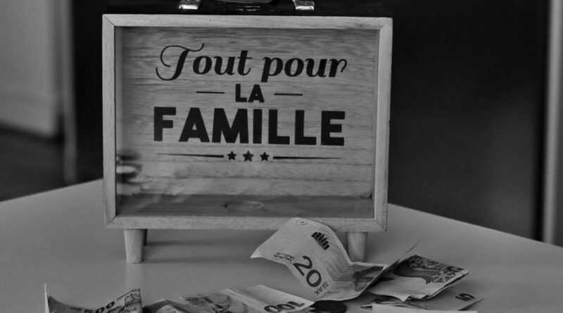 Black and white photo of a money box and various currencies on a table, symbolizing savings for family.